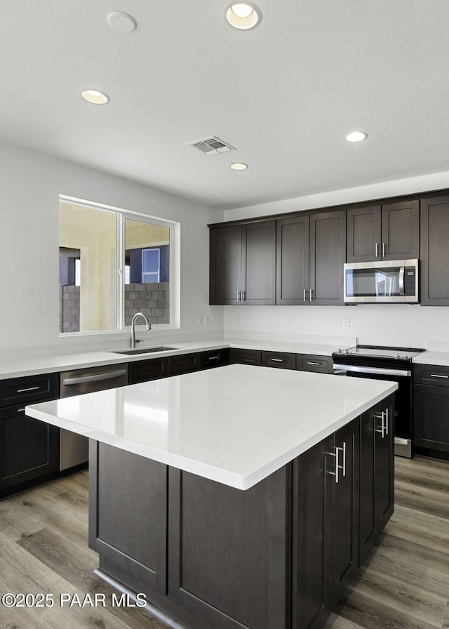 kitchen with appliances with stainless steel finishes, dark brown cabinetry, sink, hardwood / wood-style floors, and a center island