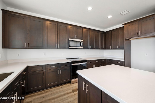 kitchen with dark brown cabinets, light hardwood / wood-style flooring, and appliances with stainless steel finishes