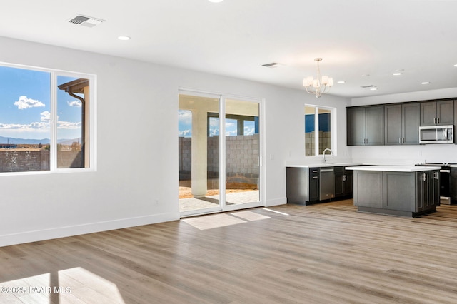 kitchen featuring light wood-type flooring, stainless steel appliances, sink, a notable chandelier, and hanging light fixtures