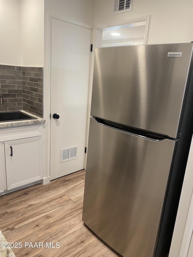 kitchen featuring a sink, freestanding refrigerator, white cabinetry, and visible vents