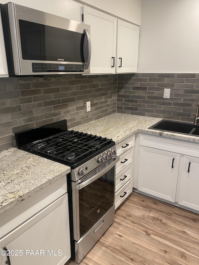 kitchen featuring a sink, appliances with stainless steel finishes, decorative backsplash, and white cabinetry