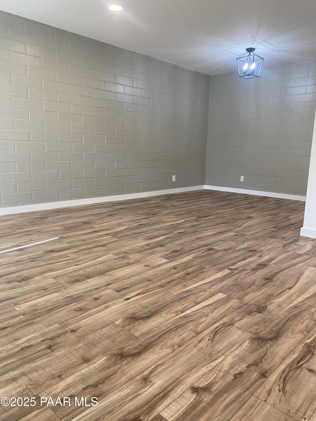 spare room featuring baseboards, wood finished floors, and concrete block wall