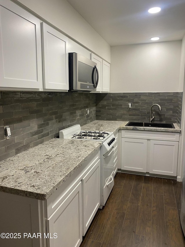kitchen with light stone countertops, a sink, white gas range, white cabinetry, and stainless steel microwave