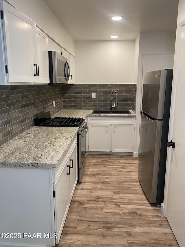 kitchen featuring decorative backsplash, white cabinets, a sink, light wood finished floors, and stainless steel appliances