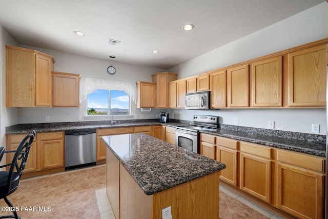 kitchen featuring a center island, sink, dark stone countertops, light tile patterned floors, and appliances with stainless steel finishes