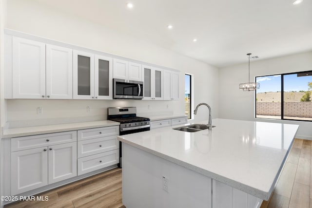 kitchen with light wood-type flooring, recessed lighting, white cabinets, a sink, and appliances with stainless steel finishes