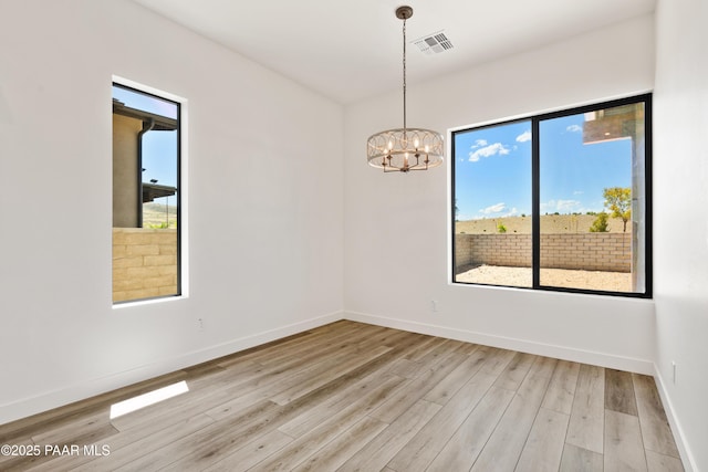 unfurnished room with visible vents, light wood finished floors, baseboards, and a chandelier