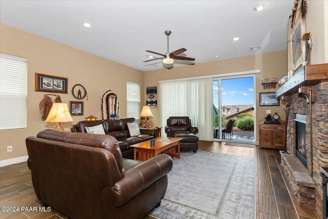 living room featuring a stone fireplace, ceiling fan, and dark wood-type flooring