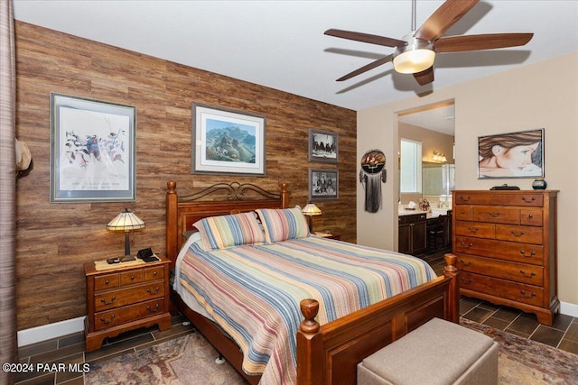 bedroom with ceiling fan, wood walls, and ensuite bath