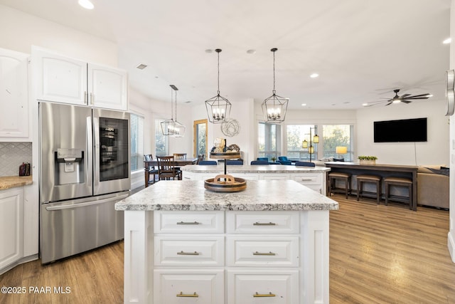 kitchen with stainless steel refrigerator with ice dispenser, pendant lighting, a center island, and white cabinets