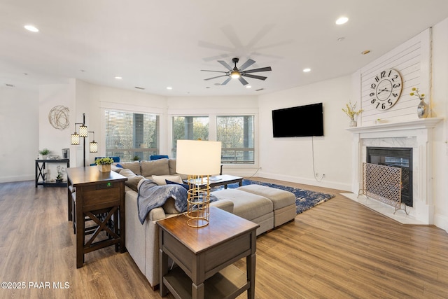 living room with wood-type flooring, ceiling fan, and a high end fireplace