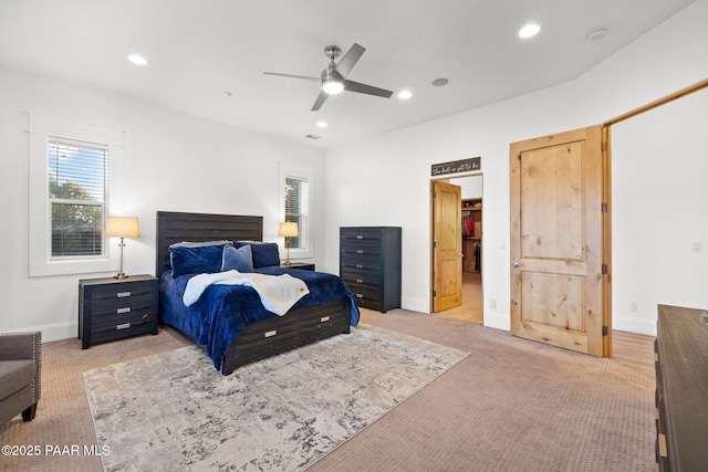 bedroom featuring ceiling fan, light colored carpet, and a walk in closet