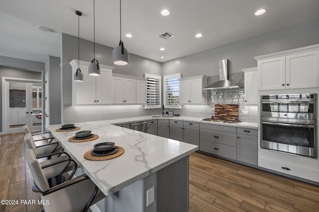 kitchen with a kitchen breakfast bar, stainless steel appliances, a sink, visible vents, and wall chimney range hood
