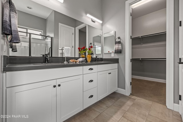 full bathroom with a stall shower, a sink, a spacious closet, baseboards, and double vanity