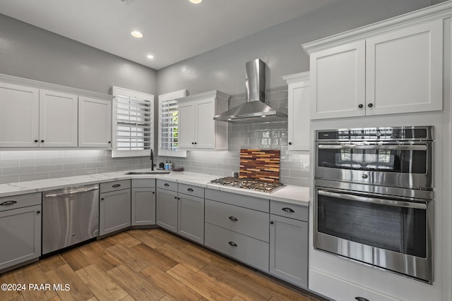 kitchen featuring a sink, stainless steel appliances, gray cabinetry, and wall chimney exhaust hood