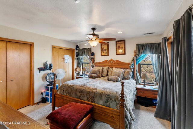 bedroom featuring ceiling fan, light colored carpet, a textured ceiling, and multiple closets