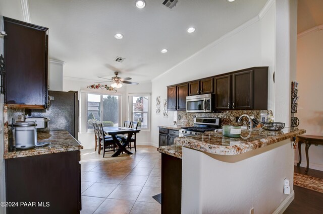 kitchen with crown molding, vaulted ceiling, appliances with stainless steel finishes, light stone counters, and kitchen peninsula