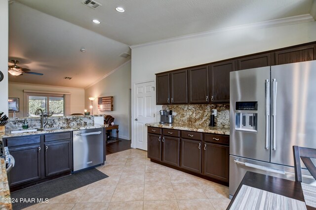 kitchen with light stone countertops, appliances with stainless steel finishes, dark brown cabinetry, vaulted ceiling, and crown molding