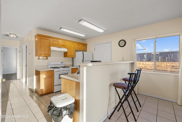 kitchen with light tile patterned floors, white appliances, and a breakfast bar area