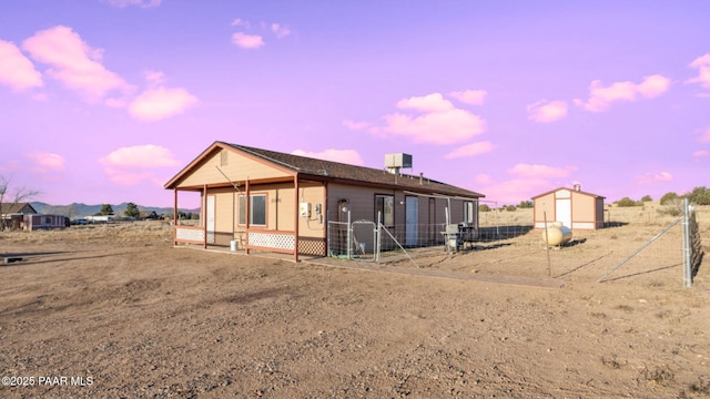 back of house at dusk featuring an outbuilding and fence