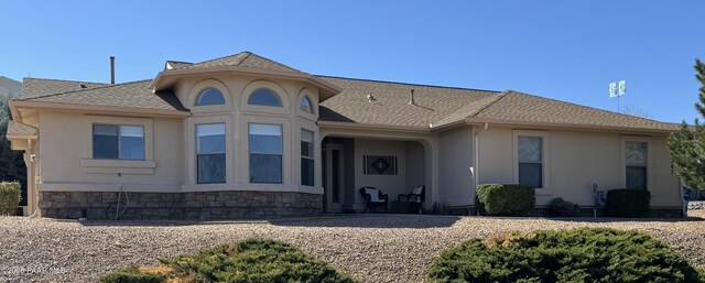 view of front facade with stucco siding, stone siding, and roof with shingles