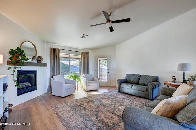 living area with a ceiling fan, a glass covered fireplace, visible vents, and wood finished floors