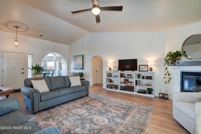 living room with ceiling fan, a multi sided fireplace, vaulted ceiling, wood finished floors, and arched walkways