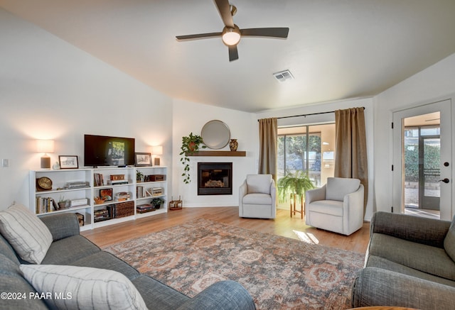 living area featuring a ceiling fan, visible vents, wood finished floors, and a glass covered fireplace