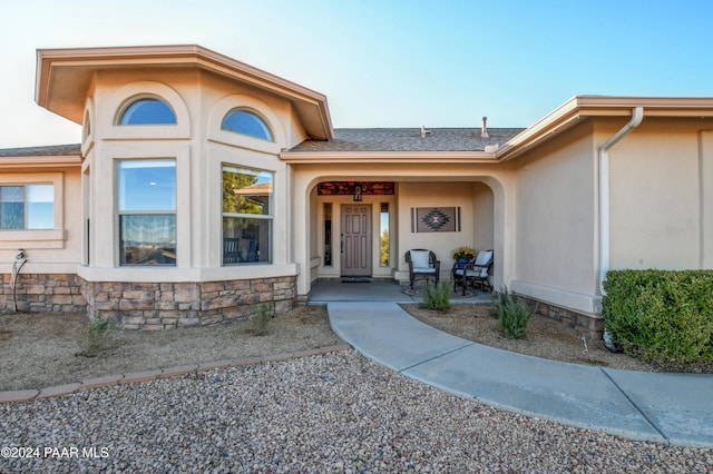 property entrance featuring stone siding, stucco siding, a porch, and roof with shingles
