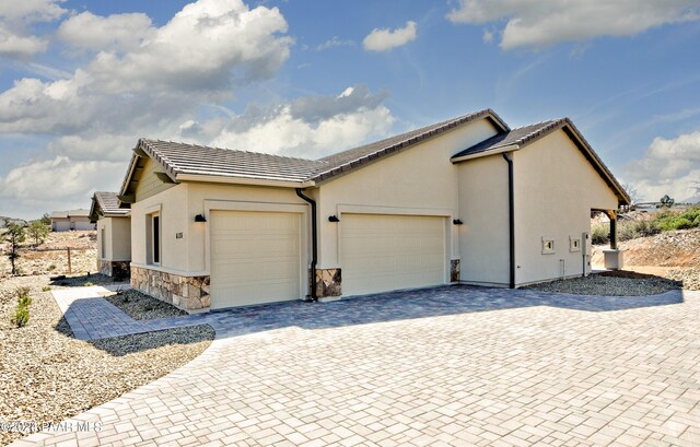 view of property exterior featuring driveway, a tile roof, a garage, stone siding, and stucco siding