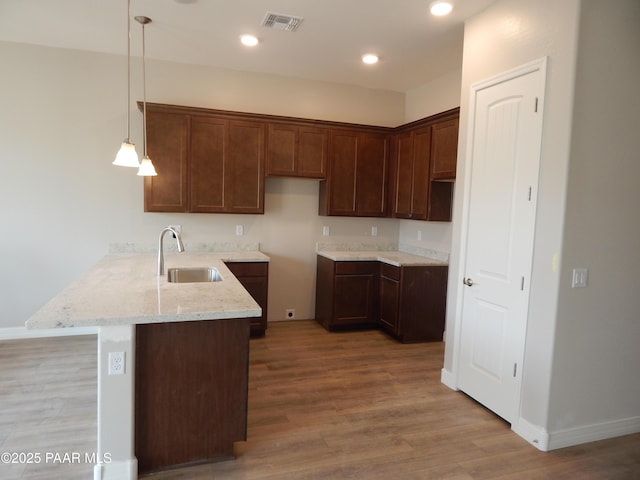 kitchen with sink, light stone counters, hanging light fixtures, light hardwood / wood-style flooring, and kitchen peninsula