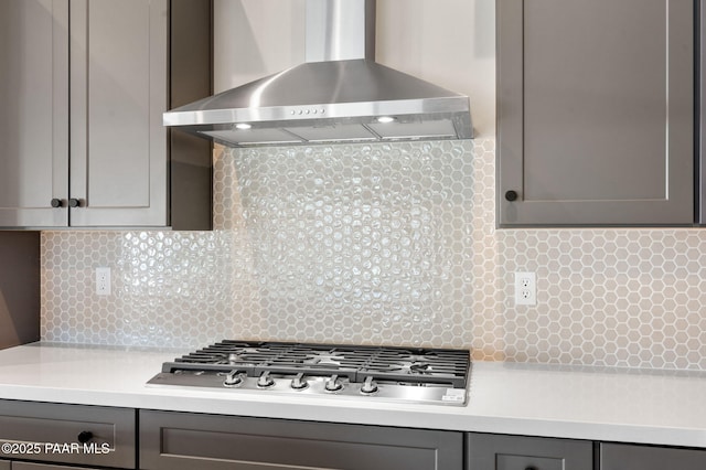 kitchen with light countertops, gray cabinets, backsplash, wall chimney range hood, and stainless steel gas cooktop