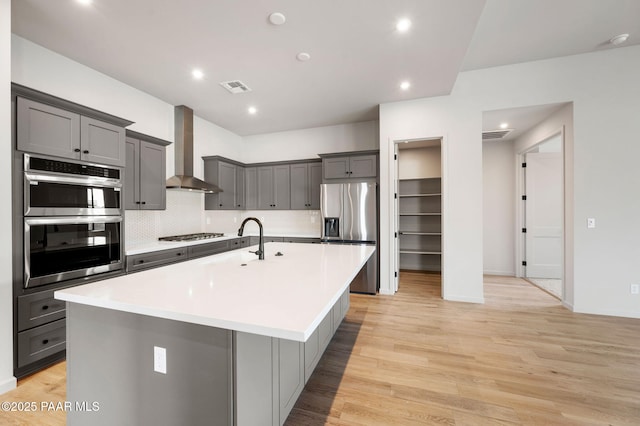 kitchen featuring gray cabinets, wall chimney exhaust hood, stainless steel appliances, and a spacious island