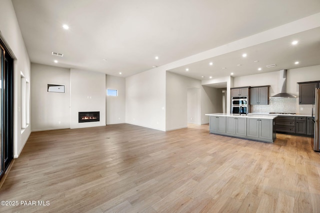 unfurnished living room featuring light wood-type flooring, recessed lighting, a glass covered fireplace, and visible vents