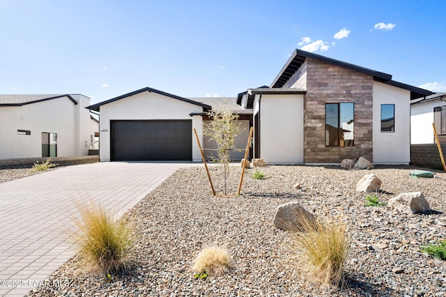 modern home with stone siding, stucco siding, decorative driveway, and a garage