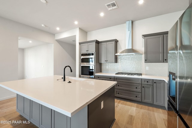 kitchen featuring stainless steel appliances, wall chimney range hood, gray cabinets, visible vents, and light wood-style flooring