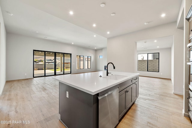 kitchen with light countertops, light wood-style flooring, a sink, open floor plan, and dishwasher