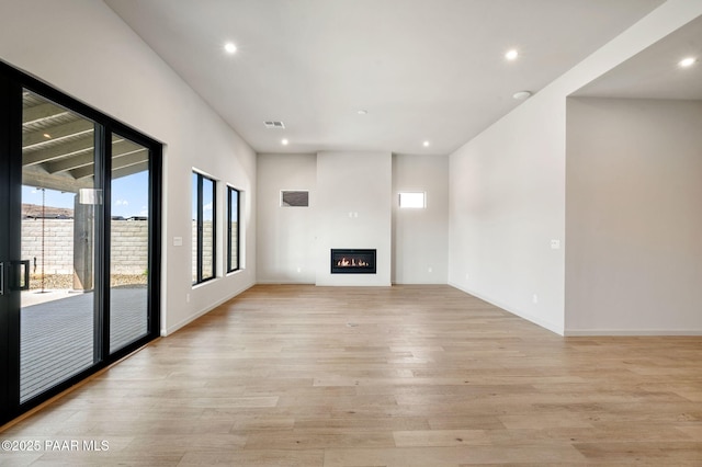 unfurnished living room with light wood-style flooring, visible vents, baseboards, a glass covered fireplace, and recessed lighting