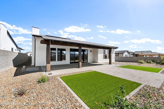 rear view of property with stucco siding, a lawn, a fenced backyard, and a patio