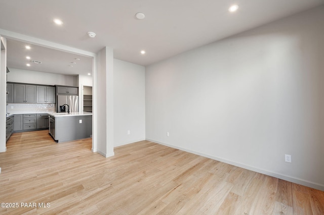 unfurnished living room featuring a sink, light wood finished floors, baseboards, and recessed lighting
