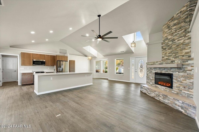 kitchen with a kitchen island with sink, ceiling fan, a fireplace, dark hardwood / wood-style flooring, and stainless steel appliances