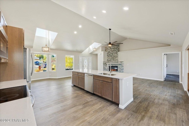 kitchen featuring light wood-type flooring, vaulted ceiling with skylight, stainless steel appliances, a kitchen island with sink, and sink