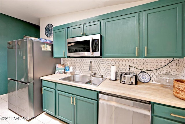 kitchen featuring backsplash, sink, green cabinetry, light tile patterned floors, and appliances with stainless steel finishes