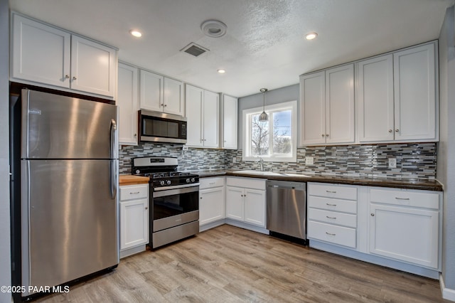 kitchen featuring visible vents, white cabinets, appliances with stainless steel finishes, decorative light fixtures, and a sink