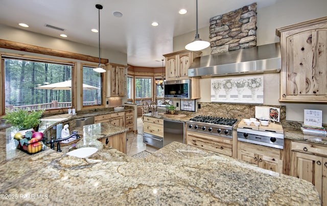 kitchen featuring light brown cabinets, hanging light fixtures, light stone countertops, a wealth of natural light, and wall chimney exhaust hood