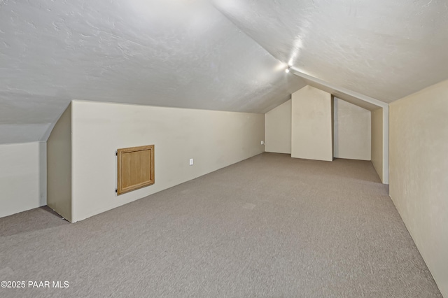 bonus room with lofted ceiling, light colored carpet, and a textured ceiling