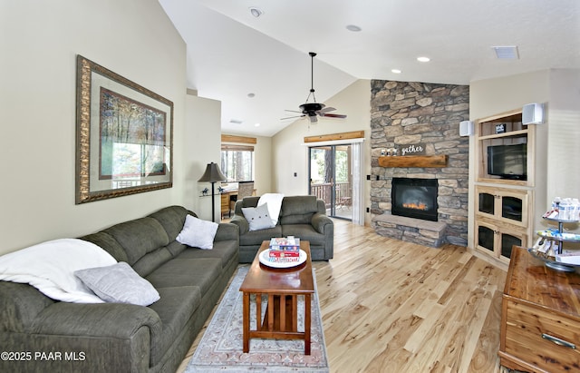 living room with light wood-type flooring, ceiling fan, vaulted ceiling, and a stone fireplace