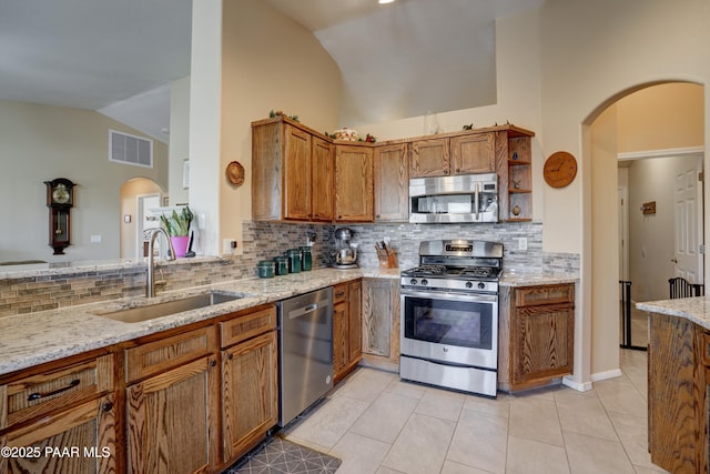 kitchen with arched walkways, brown cabinets, vaulted ceiling, stainless steel appliances, and a sink