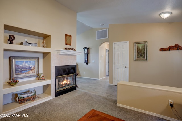 living room featuring arched walkways, lofted ceiling, visible vents, a tiled fireplace, and carpet flooring