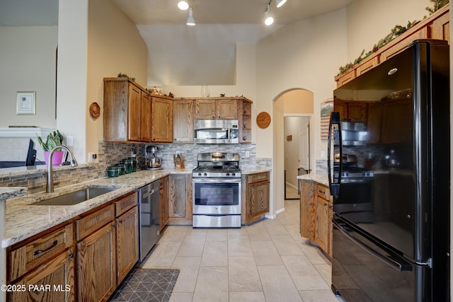 kitchen featuring arched walkways, a sink, appliances with stainless steel finishes, decorative backsplash, and brown cabinetry